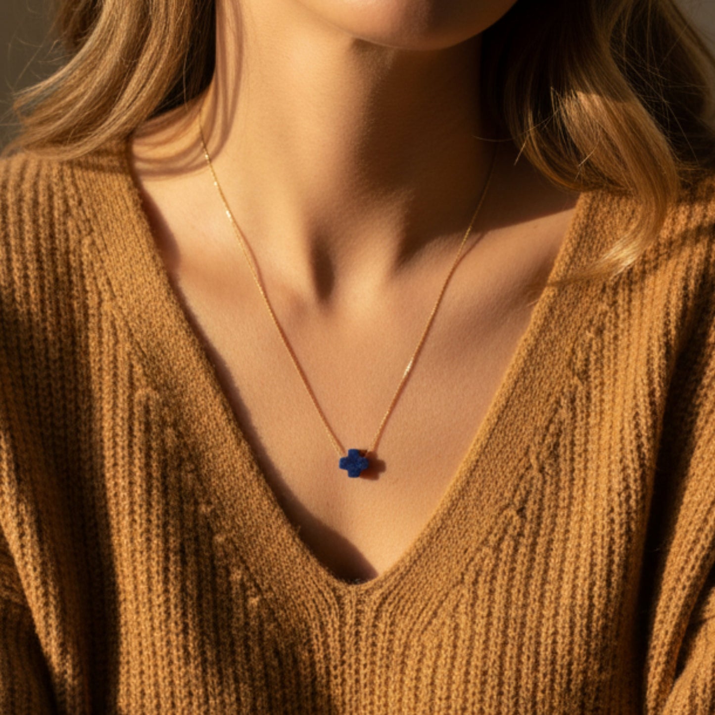 Person wearing a mustard yellow sweater with a necklace featuring a blue pendant.