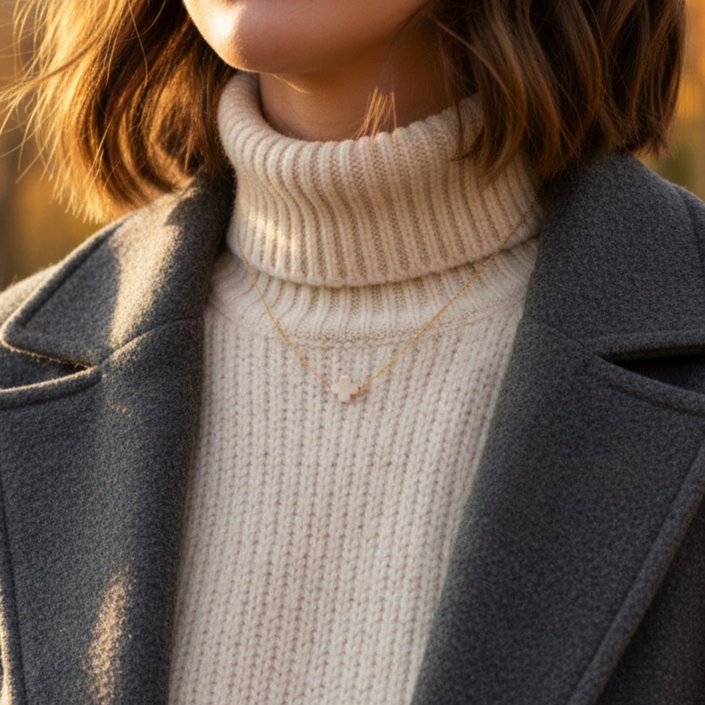 Person wearing a beige turtleneck sweater and dark coat with a blurred background