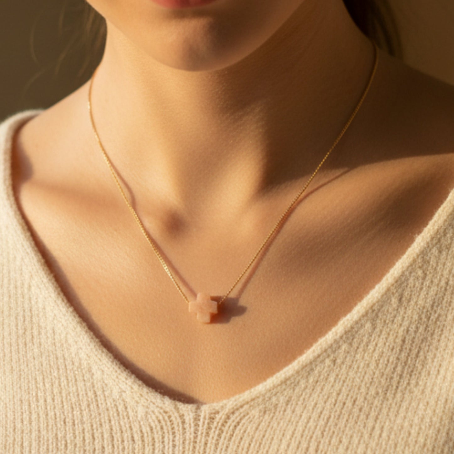 Necklace with a small pendant worn by a person in a beige sweater.